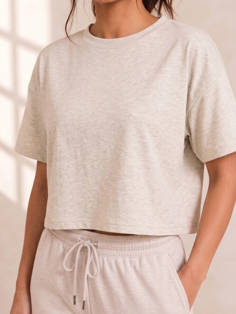 A cropped short-sleeve crewneck t-shirt in a light heathered oatmeal beige, worn by a model with matching drawstring sweatpants.