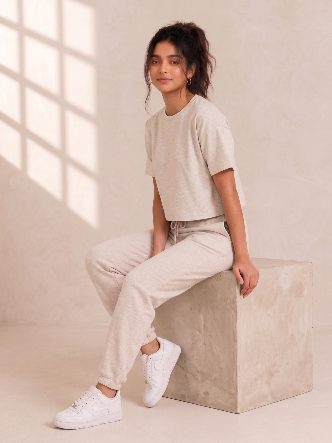 A cropped short-sleeve crewneck t-shirt in a light heathered oatmeal beige, worn by a model with matching drawstring sweatpants.