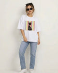 Model wearing oversized white graphic cat tee styled with straight-leg blue jeans and white sneakers.