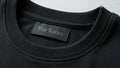 Close-up view of a minimalist black crewneck t-shirt hanging on a wooden hanger against a bright blue background.