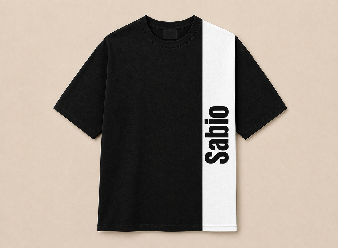 A black short-sleeve t-shirt with a bold white vertical stripe on the right side featuring the word 'Sabio' in black text, displayed flat against a light beige background.