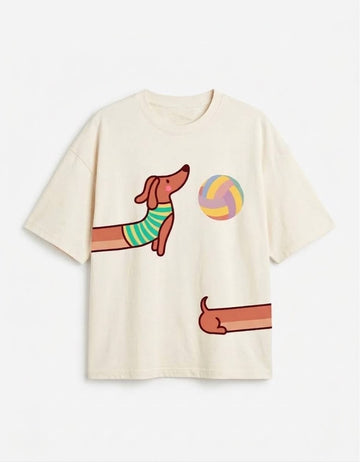 An off-white short-sleeve t-shirt featuring a cartoon graphic of a dachshund playing volleyball, with the dog's body colored in green and yellow stripes and a multi-colored volleyball.