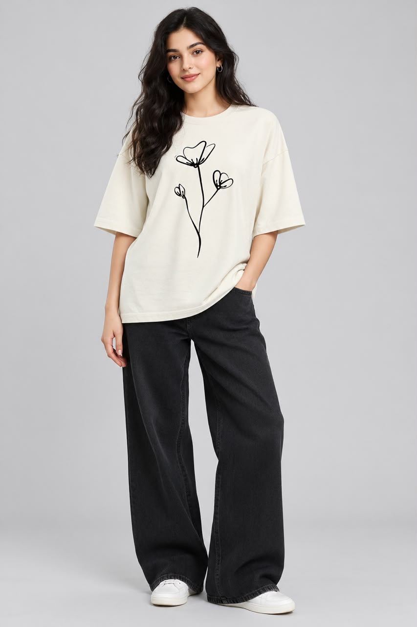 A woman modeling an oversized cream-colored t-shirt with a black line-art floral design on the front, paired with wide-leg black pants and white sneakers, against a solid light gray background.