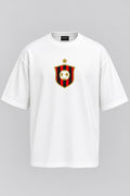 A white short-sleeve crewneck t-shirt featuring a red and black striped shield crest with a gold star and soccer ball on the chest, displayed on a neutral gray background.