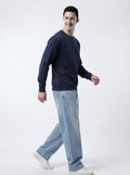 Side profile movement shot of male model wearing The Sabio solid navy blue sweatshirt and relaxed denim.