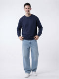 Male model wearing The Sabio navy blue relaxed fit crewneck sweatshirt paired with light wash denim jeans.