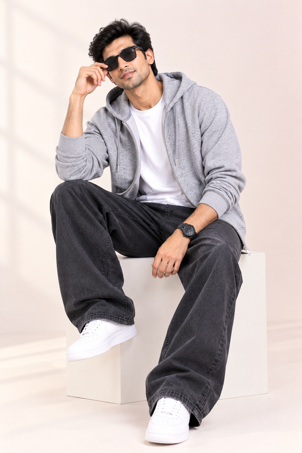 Male model seated in The Sabio Snowsoft grey heather zipper hoodie paired with baggy black denim and white sneakers.