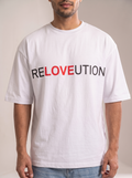 Indian male model styling The Sabio white oversized RELOVEUTION graphic tee with baggy light-wash denim, posing casually in a natural studio shot with one hand in his pocket.