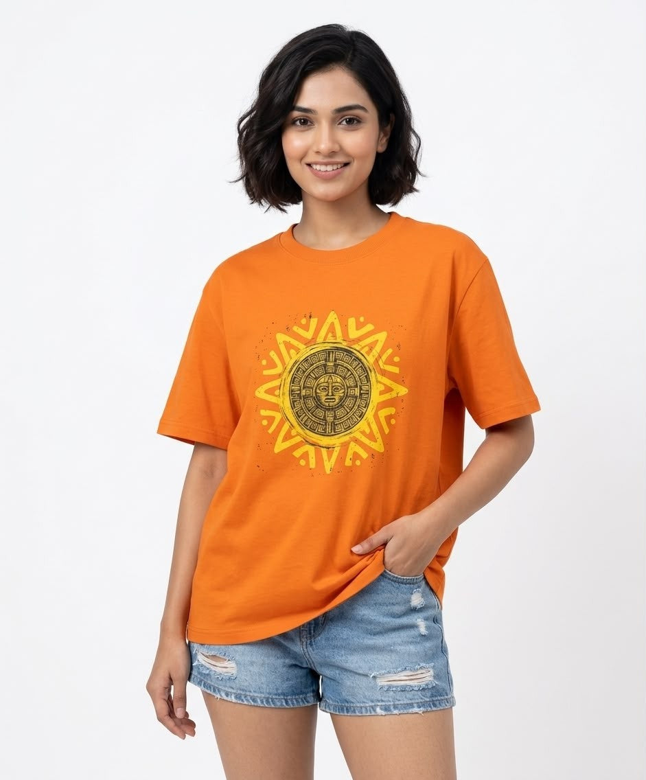 Front product view of a bright orange crewneck t-shirt featuring a circular Aztec-inspired sun face graphic in yellow and gold.